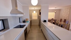 A modern kitchen with a central island, built-in oven, and a large window with blinds. - Blou Inn - Century City (Cape Town)