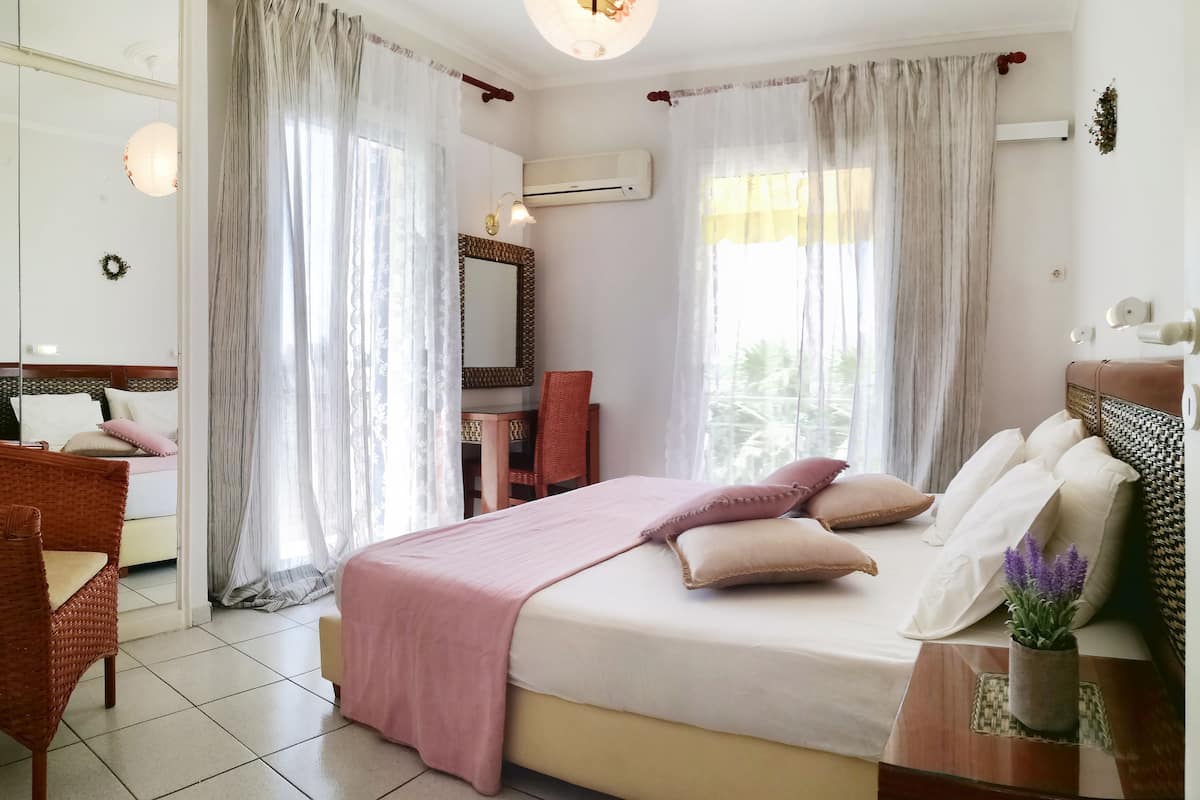 A well-lit bedroom with a bed, a chair, a desk, and a mirror.