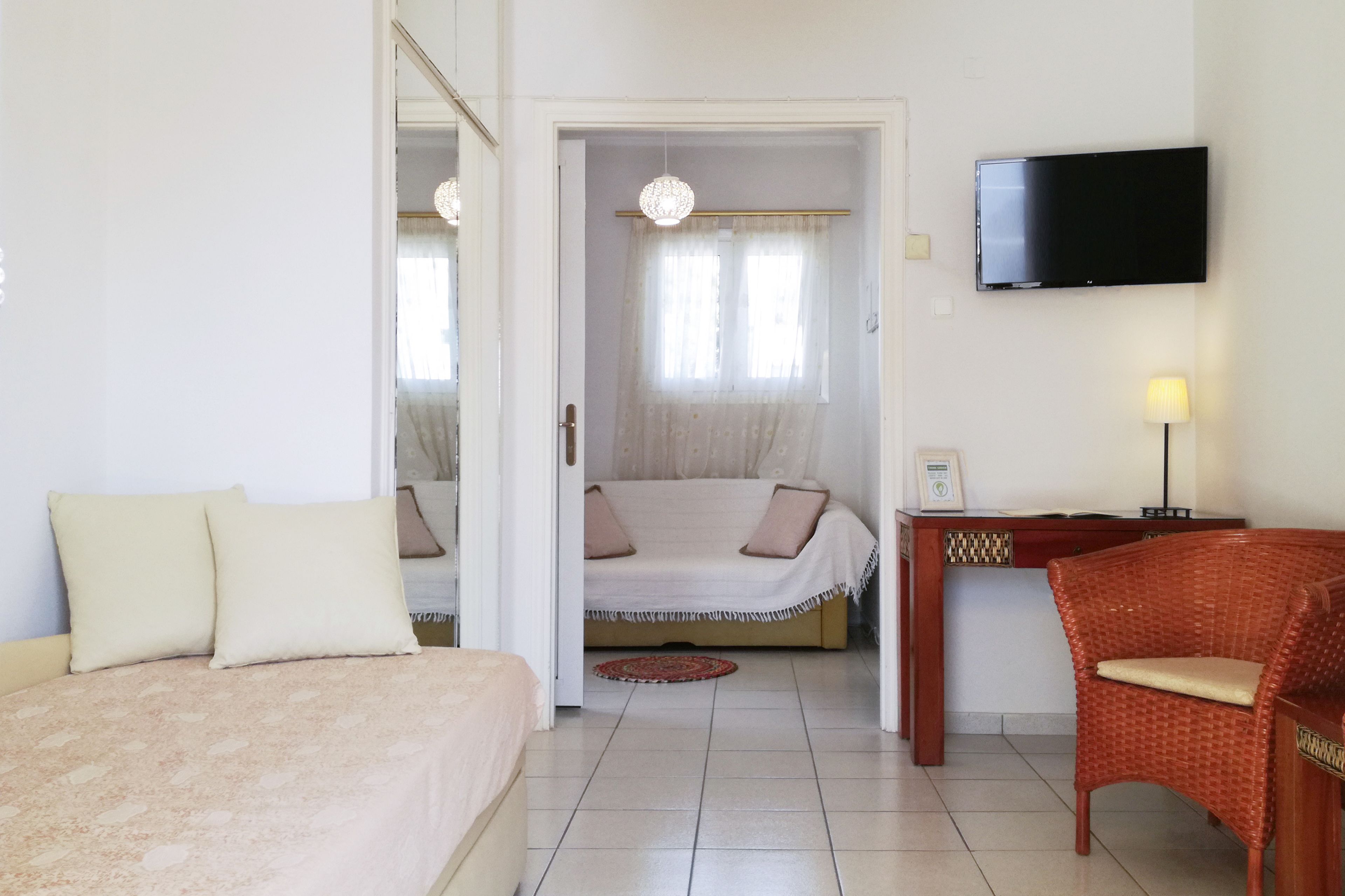 Quarto de hotel com cama, sofá, cadeira de vime, escrivaninha, televisão e janela com cortinas.