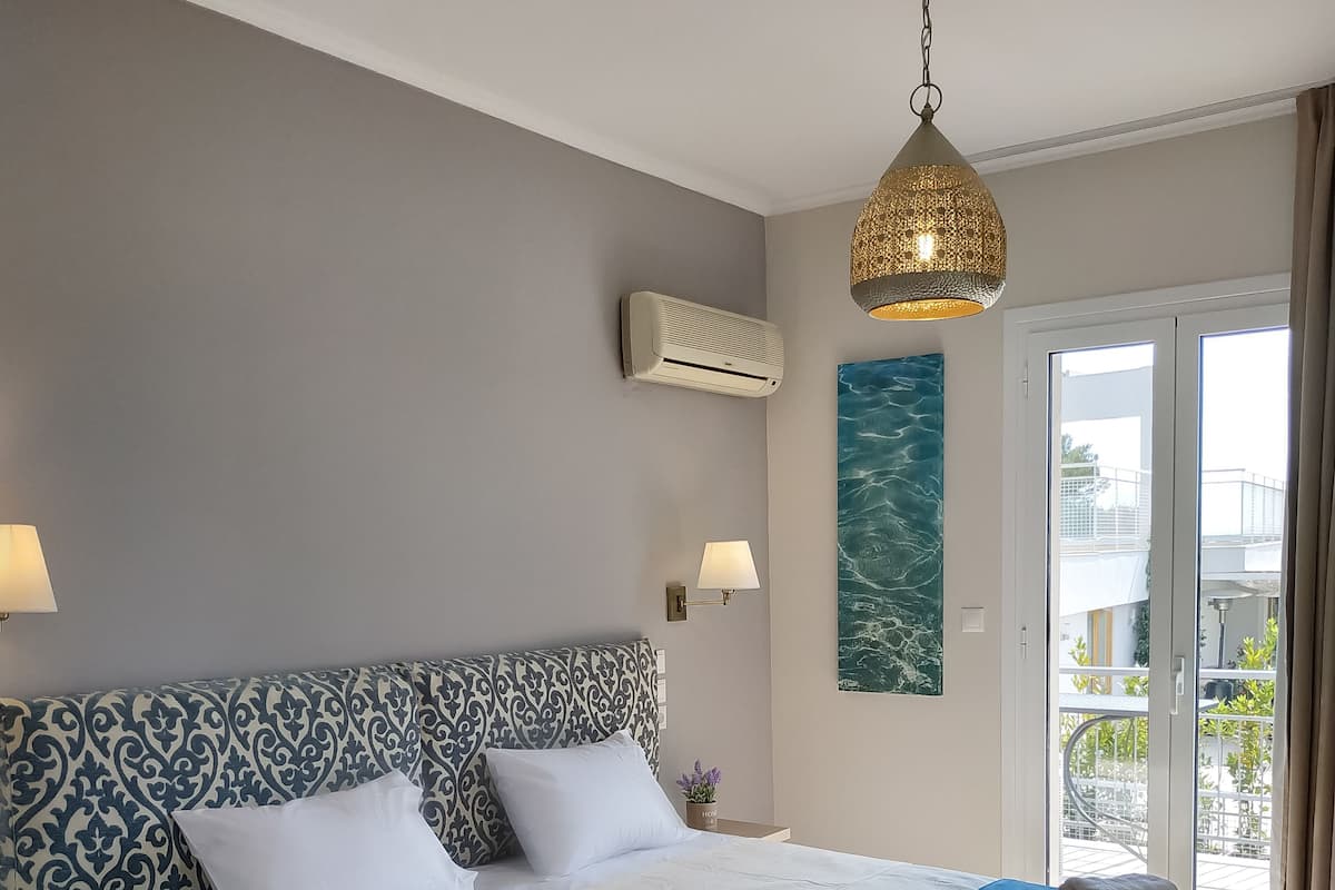 A hotel room with a large bed, a ceiling fan, an air conditioning unit, a view of the outside balcony, and a decorative wall piece.