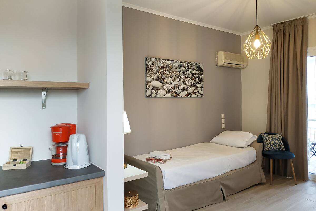 A bedroom with a bed, a coffee maker, a lamp, a shelf with glasses, and a painting on the wall.