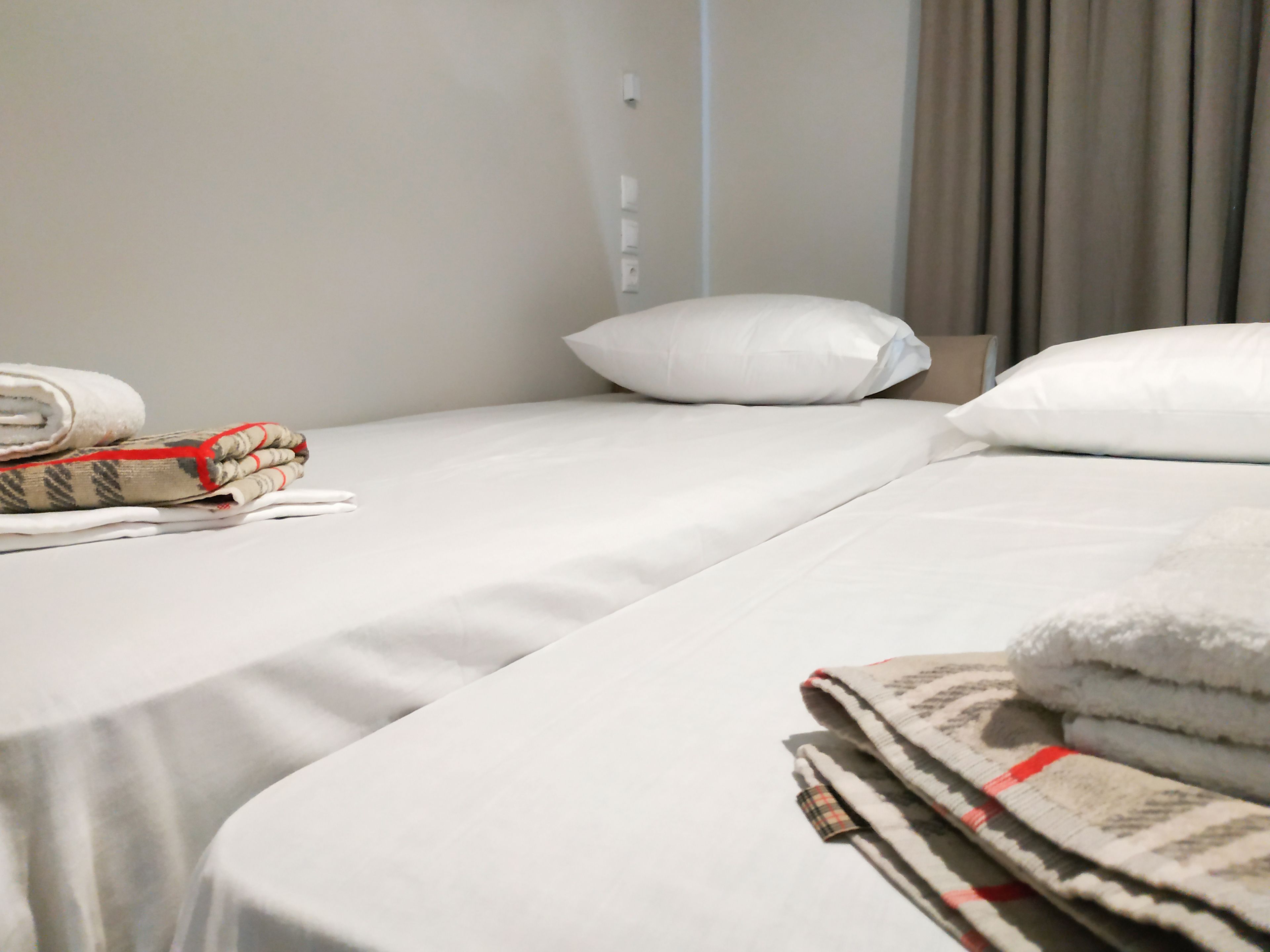 Ein Hotelzimmer mit einem ordentlich bezogenen Bett, einer gefalteten Decke und einem zusammengerollten Handtuch auf dem Bett.