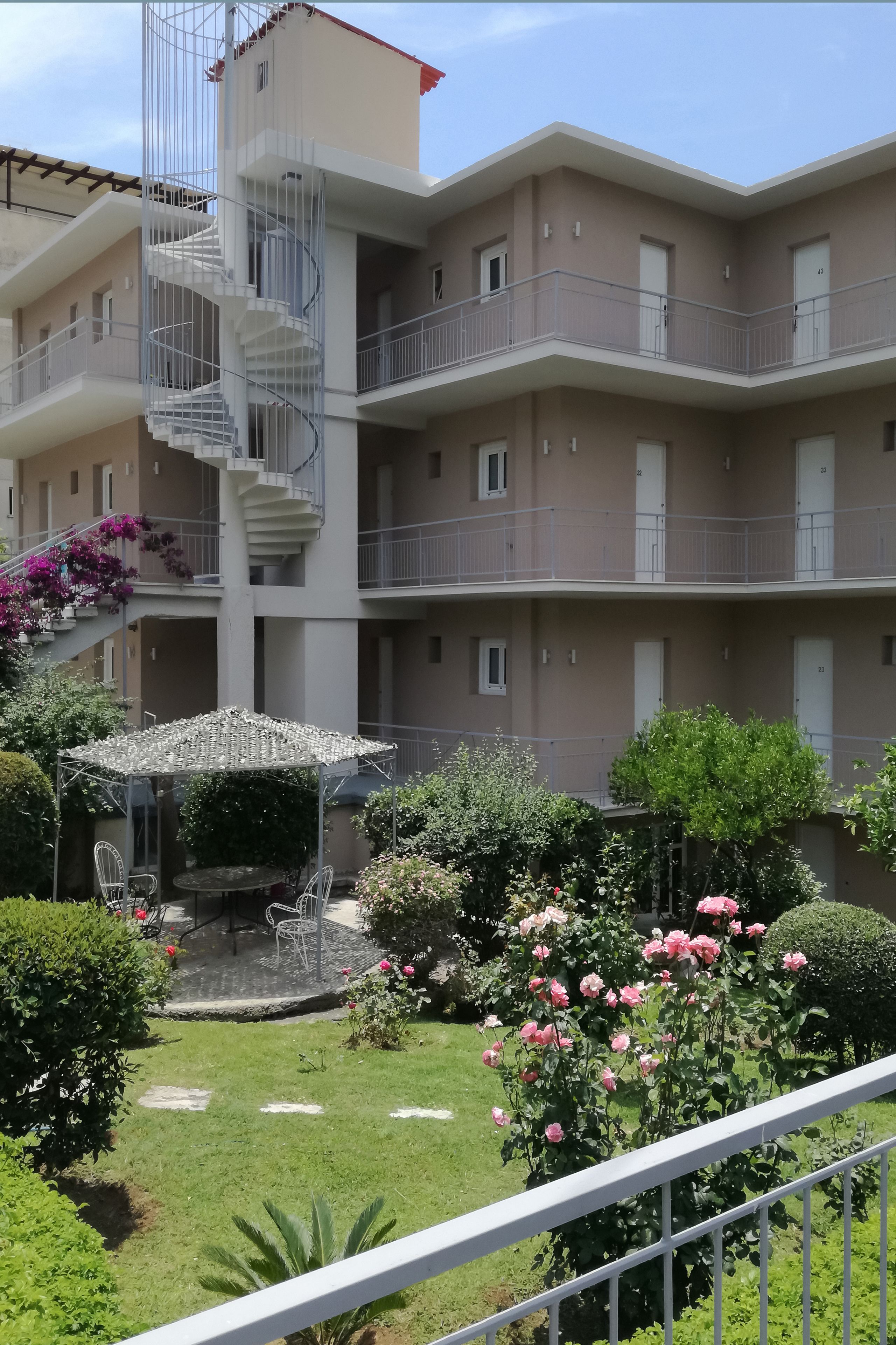 Un edificio residencial de varios pisos con balcones, una escalera en espiral central y un pequeño patio con mobiliario exterior.
