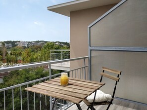 A balcony with a wooden table and chair, a white cushion, and a glass of orange juice. - Lilly Apartments (Vari-Voula-Vouliagmeni)