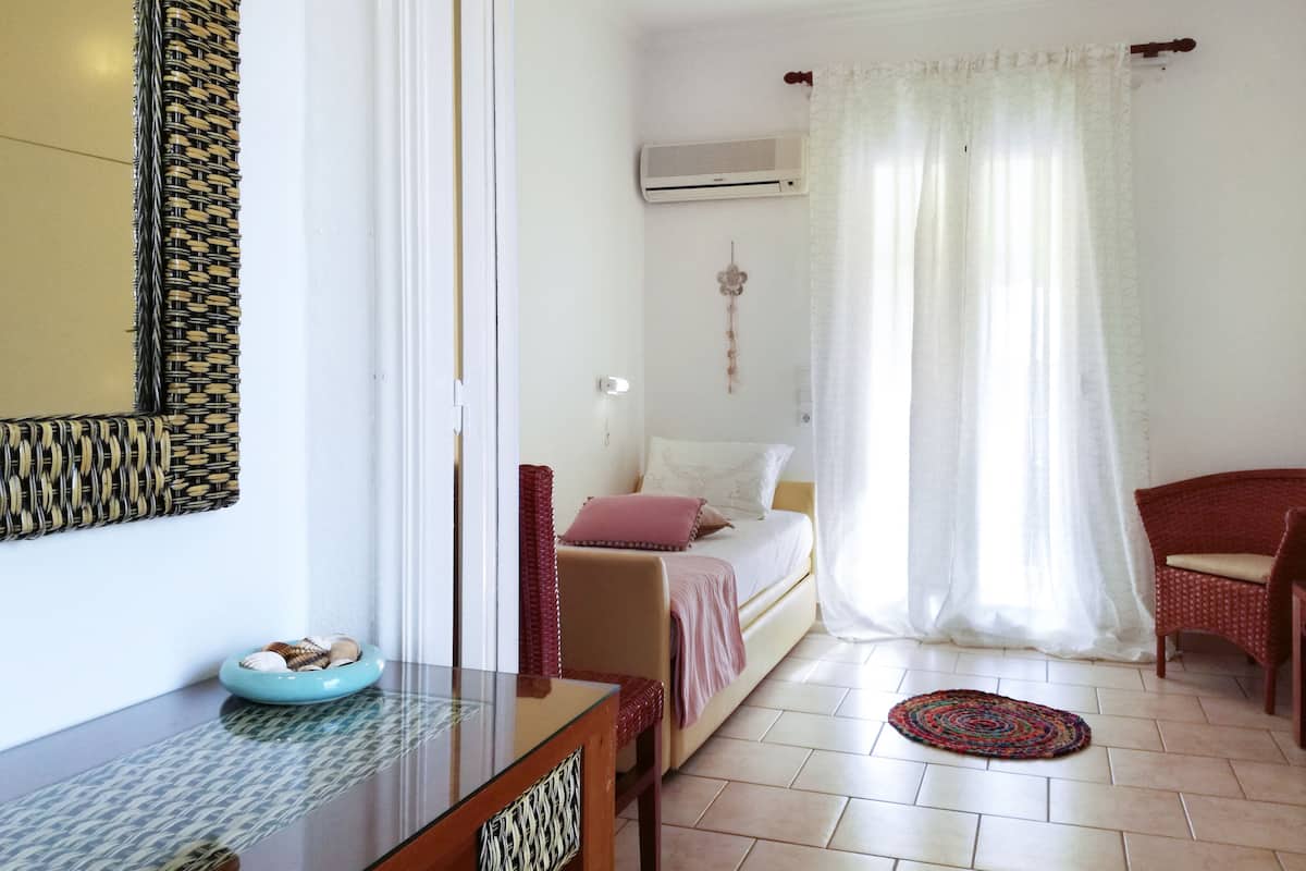 A bedroom with a bed, a chair, a table, and a wall-mounted air conditioner.