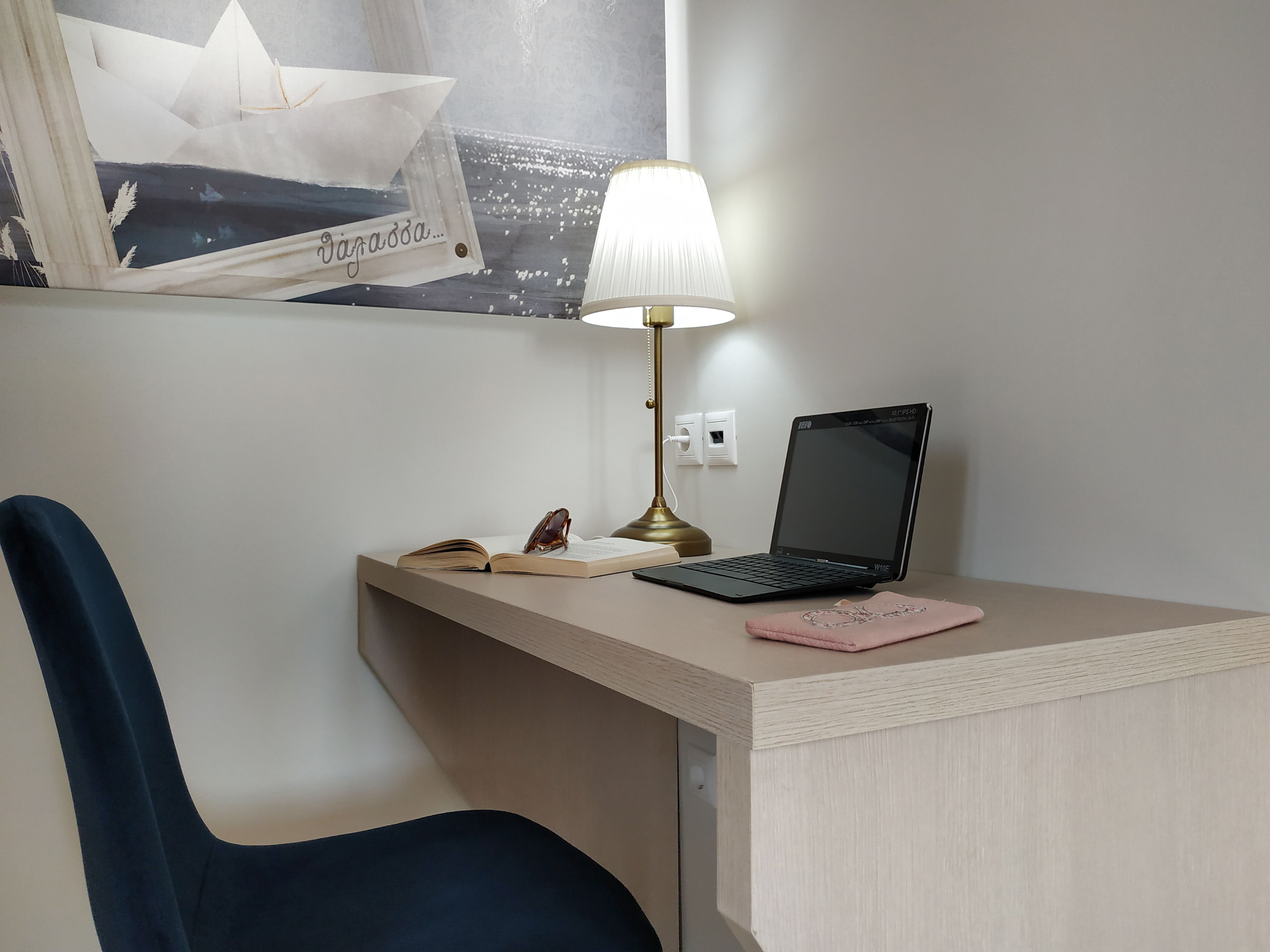 Un bureau avec un ordinateur portable, une lampe, une paire de lunettes et un carnet rose.