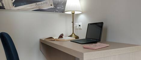 Un bureau avec un ordinateur portable, une lampe, une paire de lunettes et un carnet rose.