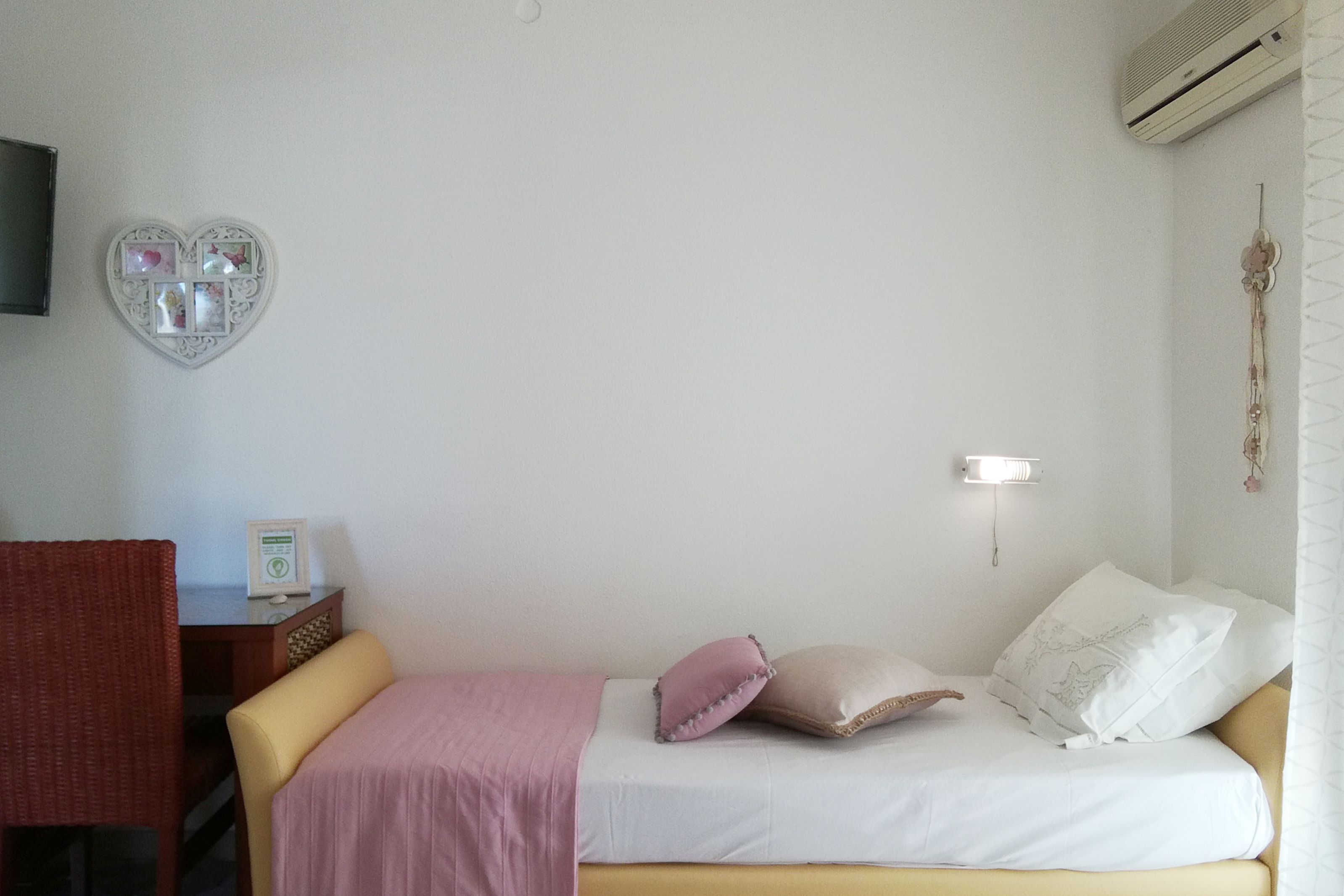 Een slaapkamer met een bed, een bureau, een stoel, een aan de muur bevestigde televisie en een decoratieve hartvormige decoratie.
