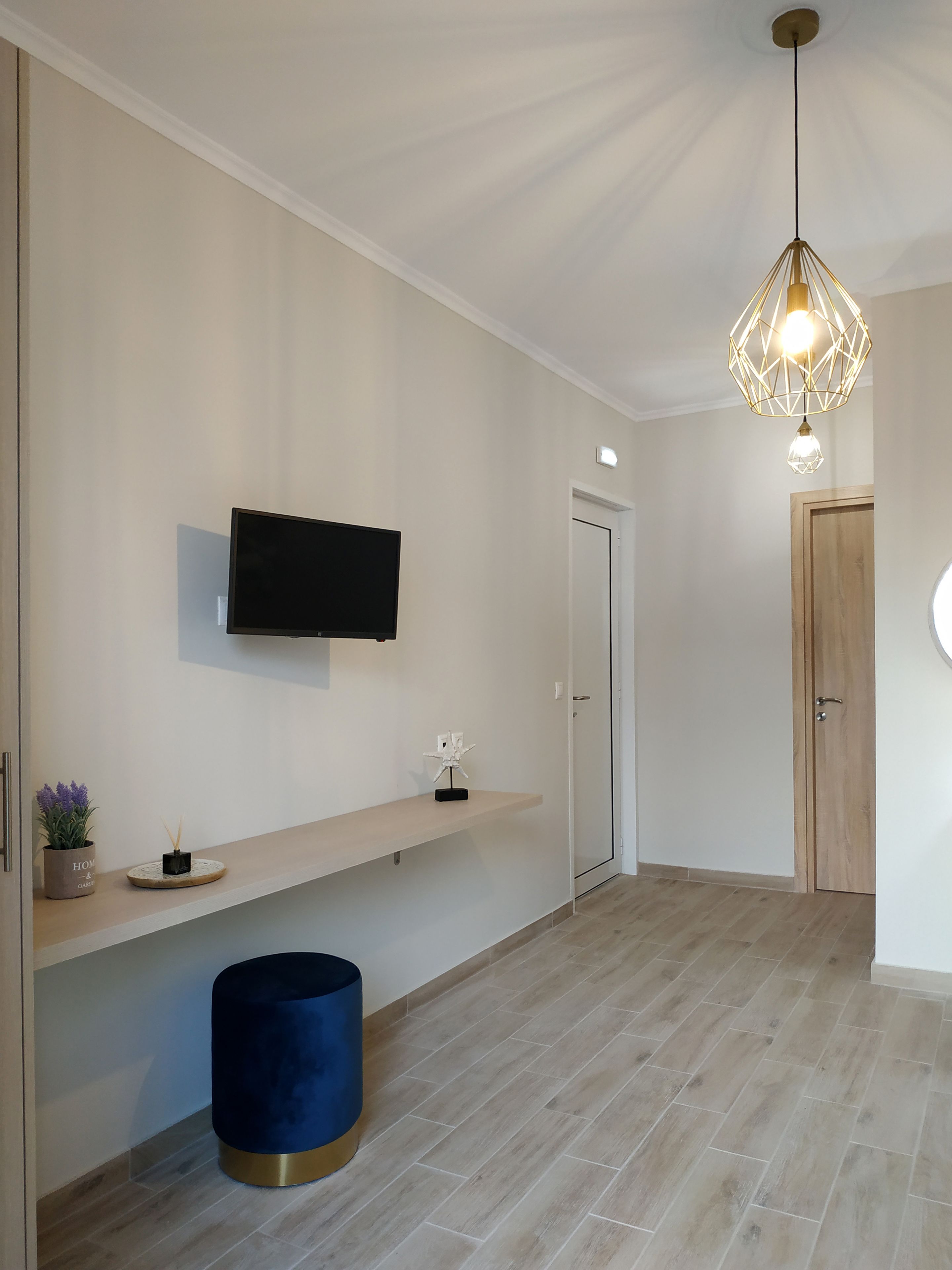 Un couloir moderne avec un téléviseur à écran plat fixé au mur, une porte en bois, un objet cylindrique bleu et une suspension lumineuse.