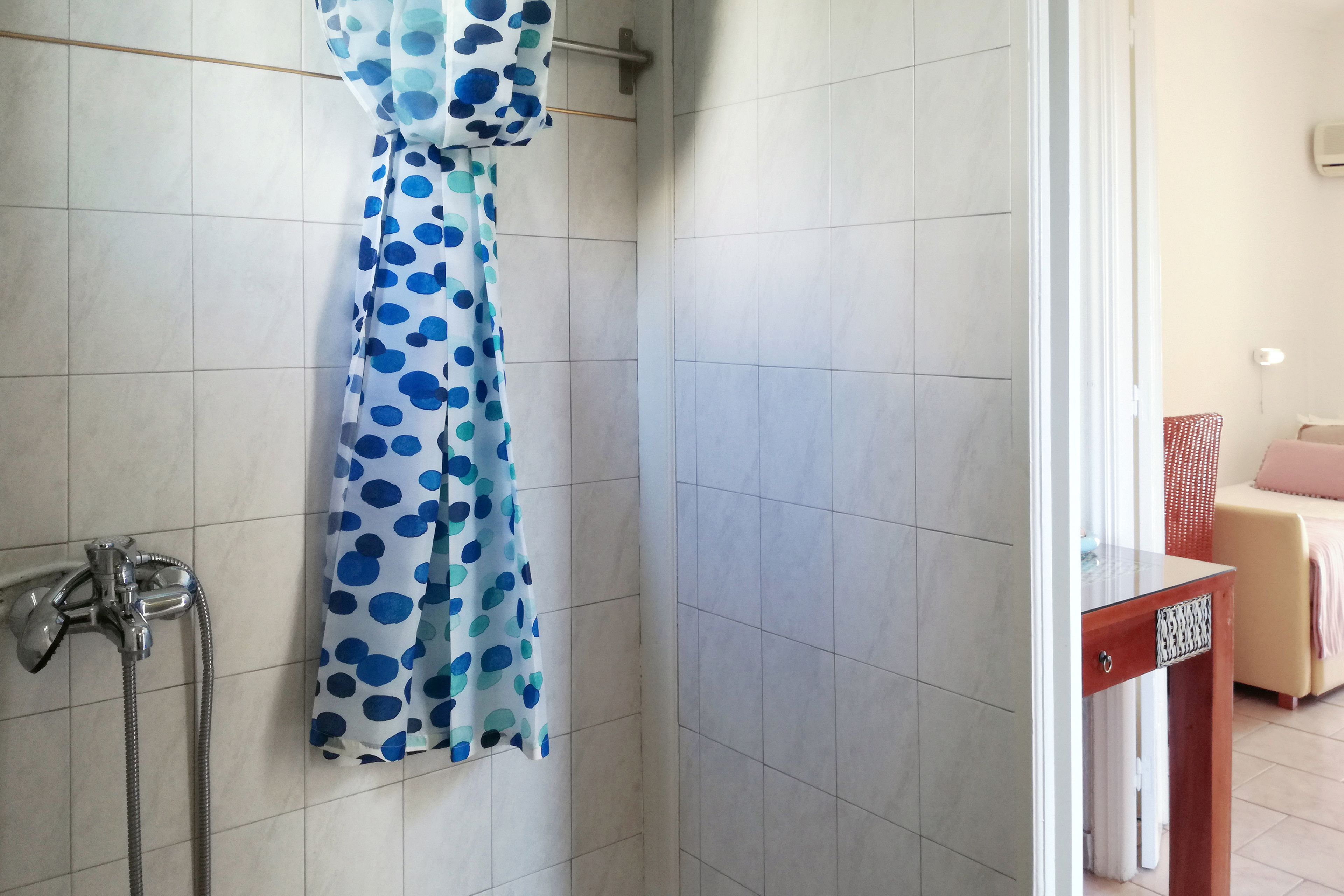 A bathroom with a shower, a towel rack with a polka dot towel, and a wooden side table with a decorative drawer.