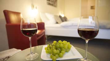 A room with a bed, a red chair, a table with two wine glasses and a plate of grapes.