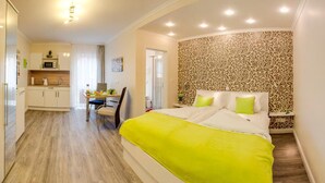 A modern hotel room with a large bed, a dining area, and a kitchenette. - Wehyer Aparthotel (Weyhe)