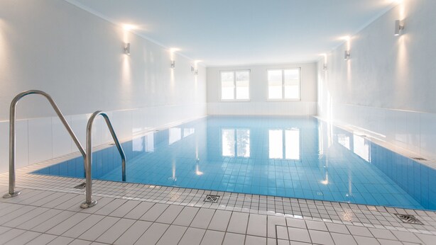 An indoor swimming pool with clear blue water, tiled walls, and a metal ladder. - Wehyer Aparthotel (Weyhe)