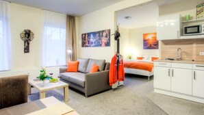 A modern living room with a sofa, a coffee table, and a dining area. There is a kitchen with white cabinets and a microwave. - Wehyer Aparthotel (Weyhe)