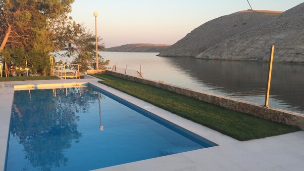 A rectangular swimming pool with a clear blue water surface, surrounded by a paved deck. - Villa Nika (Pag)