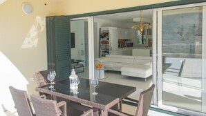 An open sliding glass door leading to a living area with a white sofa, a dining table with wicker chairs, and a kitchen in the background. - Villa Nika (Pag)
