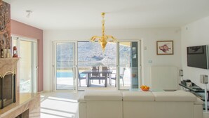 A modern living room with a large window, a chandelier, a dining area, and a view of a mountainous landscape. - Villa Nika (Pag)