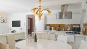A modern kitchen with white cabinets, a stainless steel range hood, and a dining area with a round table and white chairs. - Villa Nika (Pag)