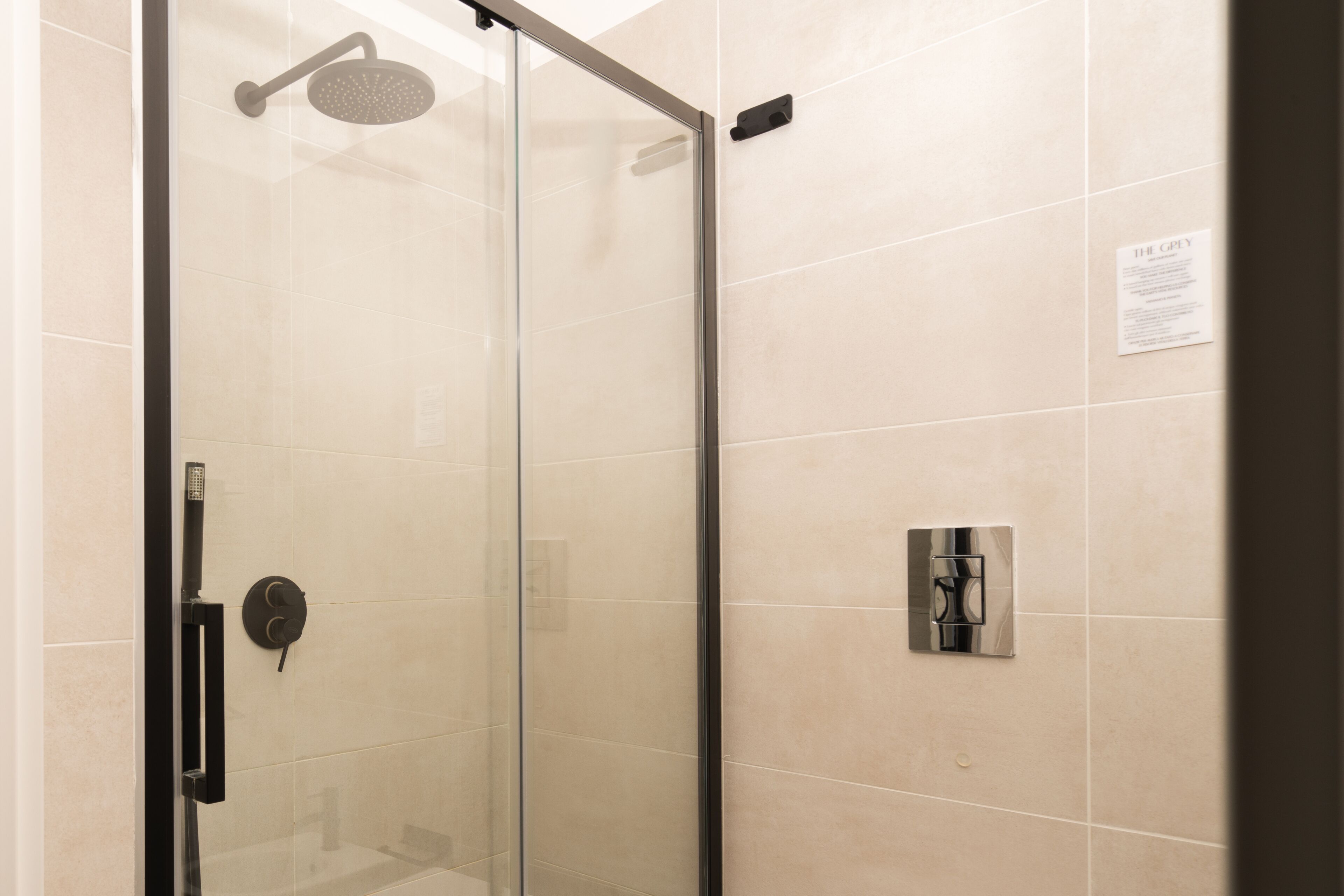 A glass-enclosed shower with a handheld showerhead and a wall-mounted control panel.