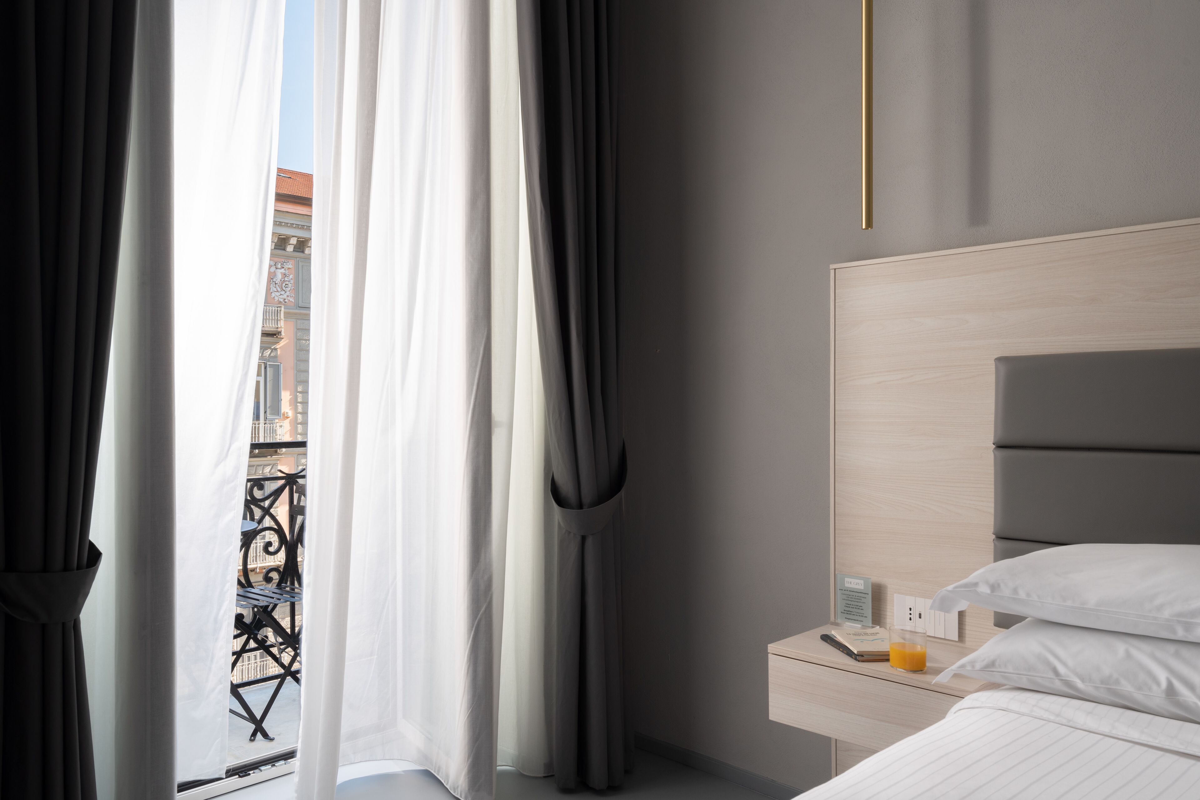 A hotel room with a bed, a bedside table with a phone and a glass of orange juice, and a view of the outside balcony.