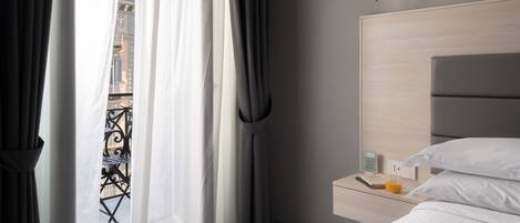 A hotel room with a bed, a bedside table with a phone and a glass of orange juice, and a view of the outside balcony.