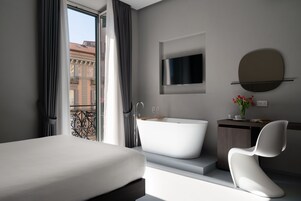 Een moderne hotelkamer met een groot bed, een vrijstaand bad, een minimalistische wastafel en een groot raam met uitzicht op de stad.