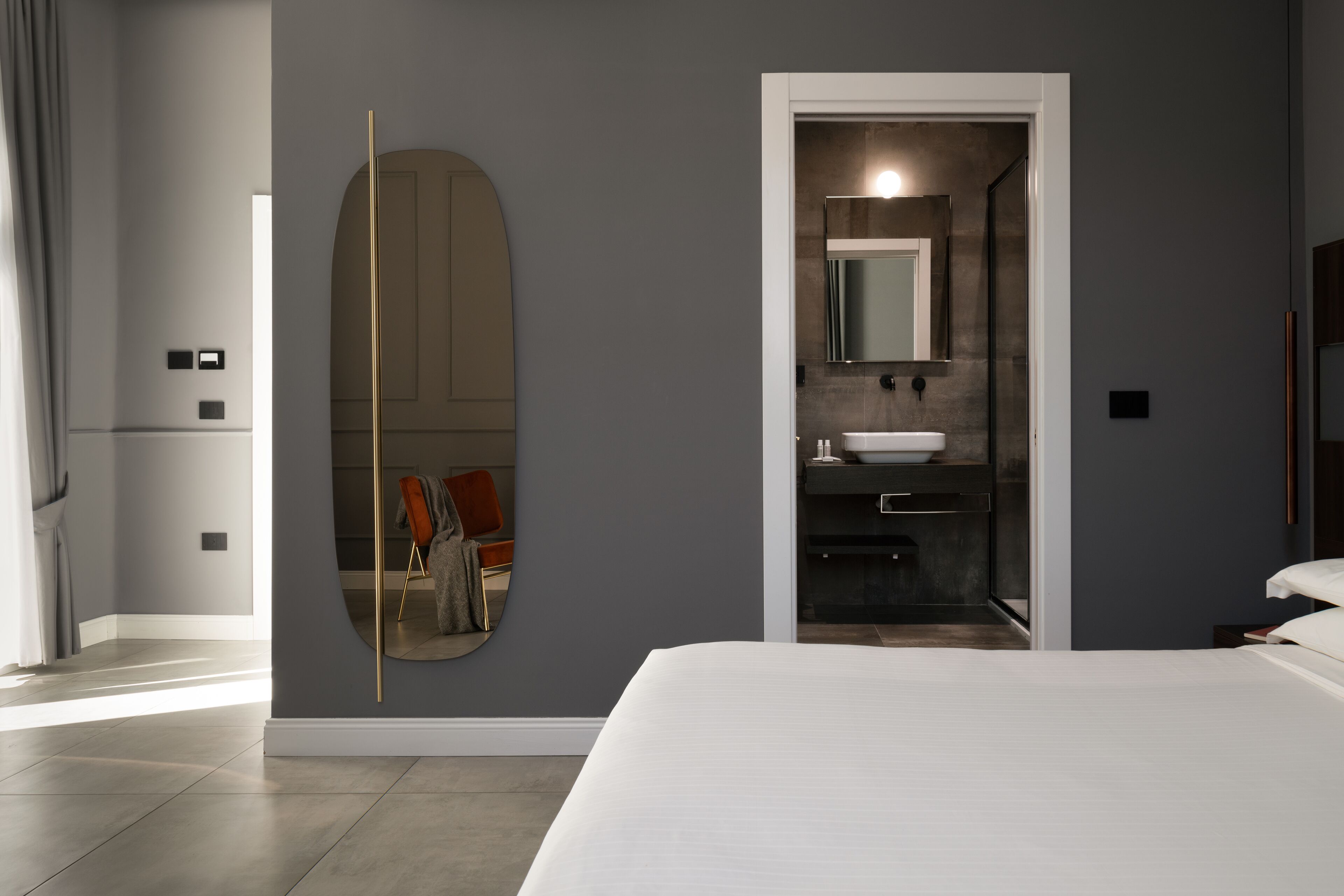 A modern hotel room with a large bed, a bathroom with a sink and mirror, and a large mirror on the wall.