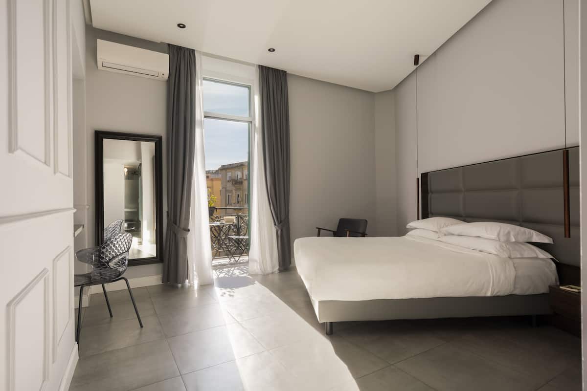 A modern hotel room with a large bed, a chair, a desk, and a view of the outside.