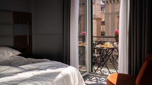 A hotel room with a bed, a balcony with a table and chairs, and a view of the cityscape. - The Grey (Naples)