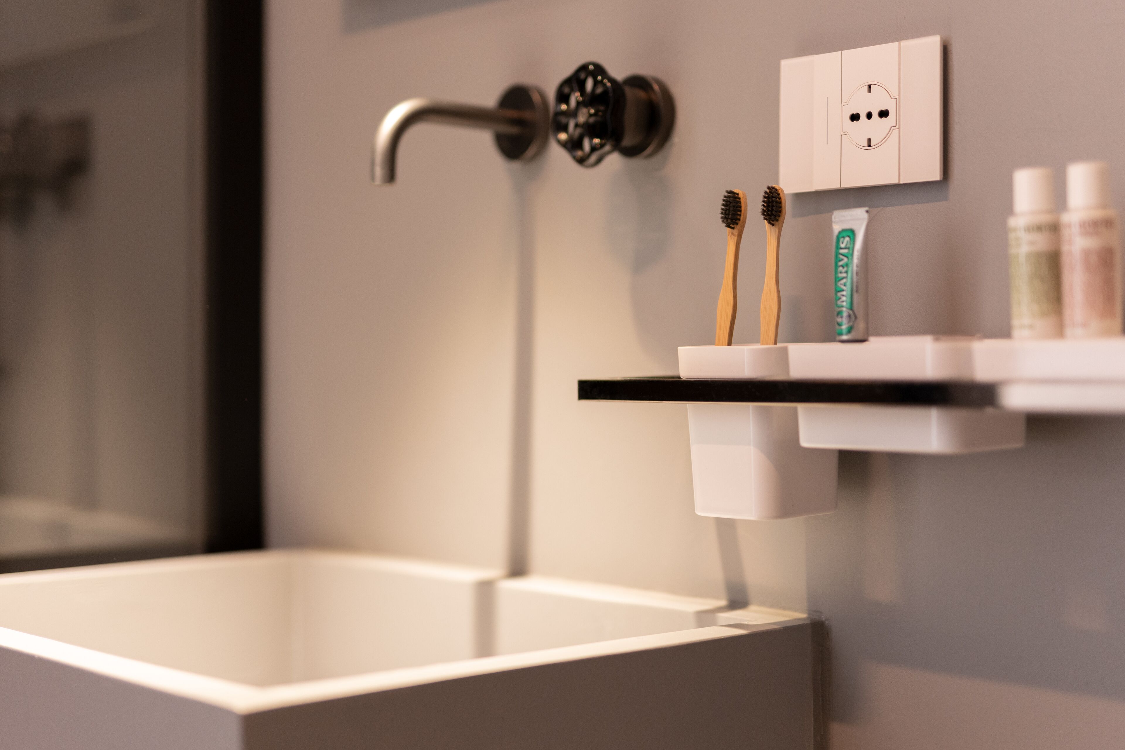 A modern bathroom with a white sink, a mounted faucet, and a shelf with toothbrushes and toothpaste.