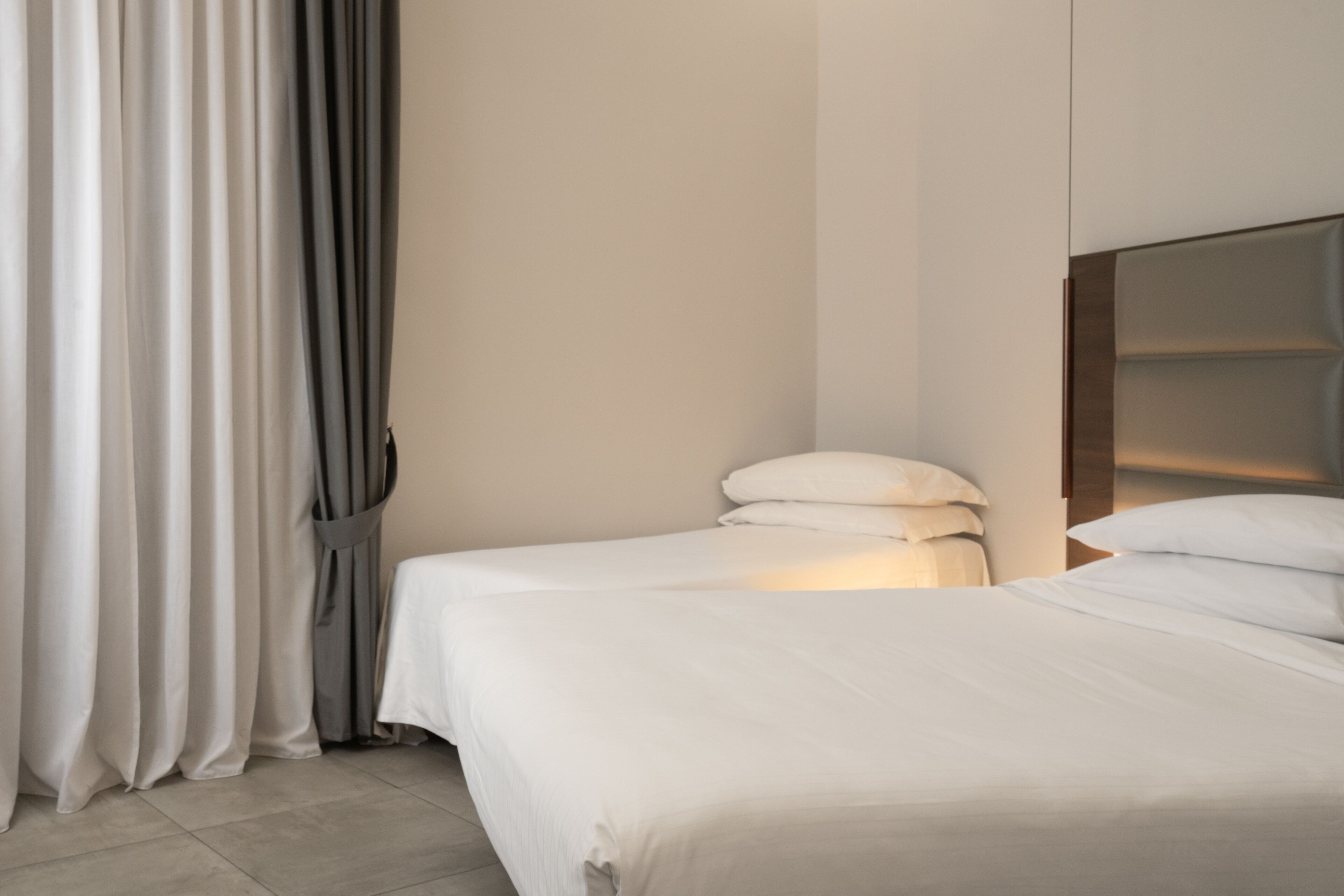 A modern hotel room with a large bed, a headboard, and a curtain.