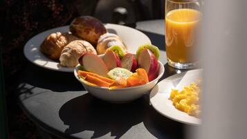 A table with croissants, a bowl of fruit, scrambled eggs, and a glass of orange juice.