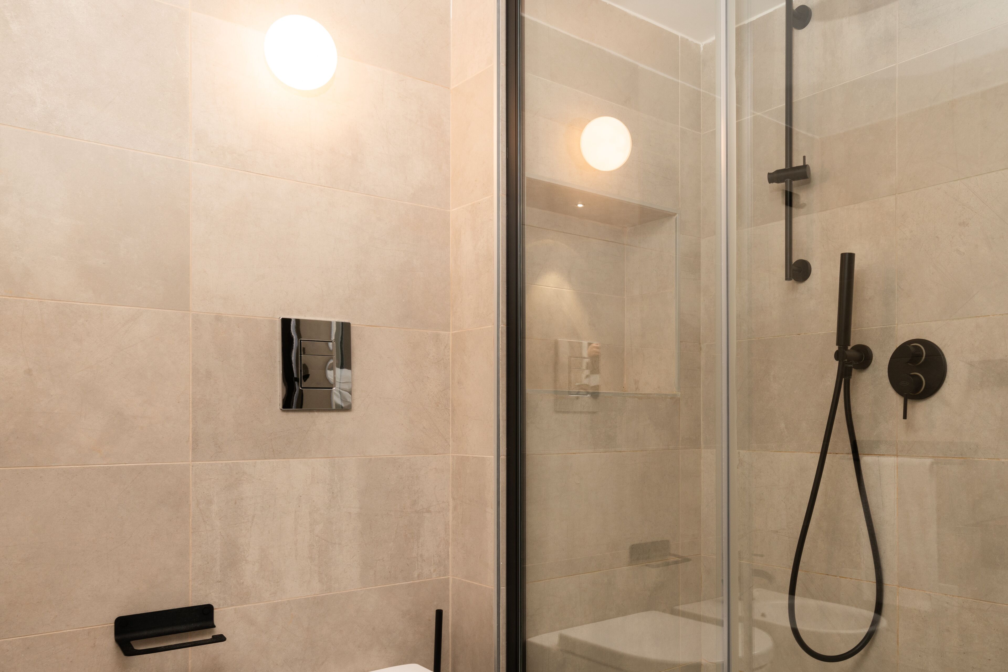 Une salle de bain moderne dotée d’une douche à parois de verre, d’un pommeau de douche à main et d’un robinet mural.