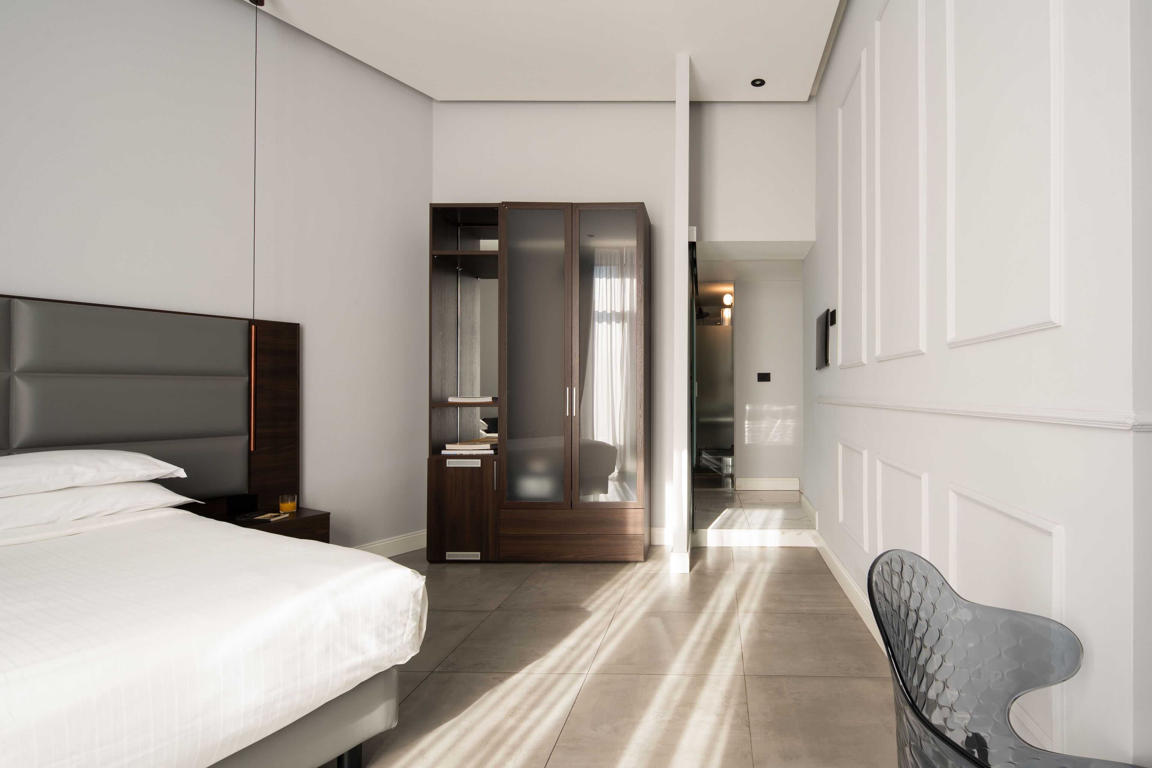 Ein modernes Hotelzimmer mit einem großen Bett, einem Schrank, einer Sitzecke und Blick in die Diele.