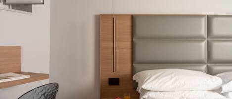 A modern bedroom with a wooden headboard, a glass chair, a bedside table with a book and a glass of orange juice, and a bed with white bedding.