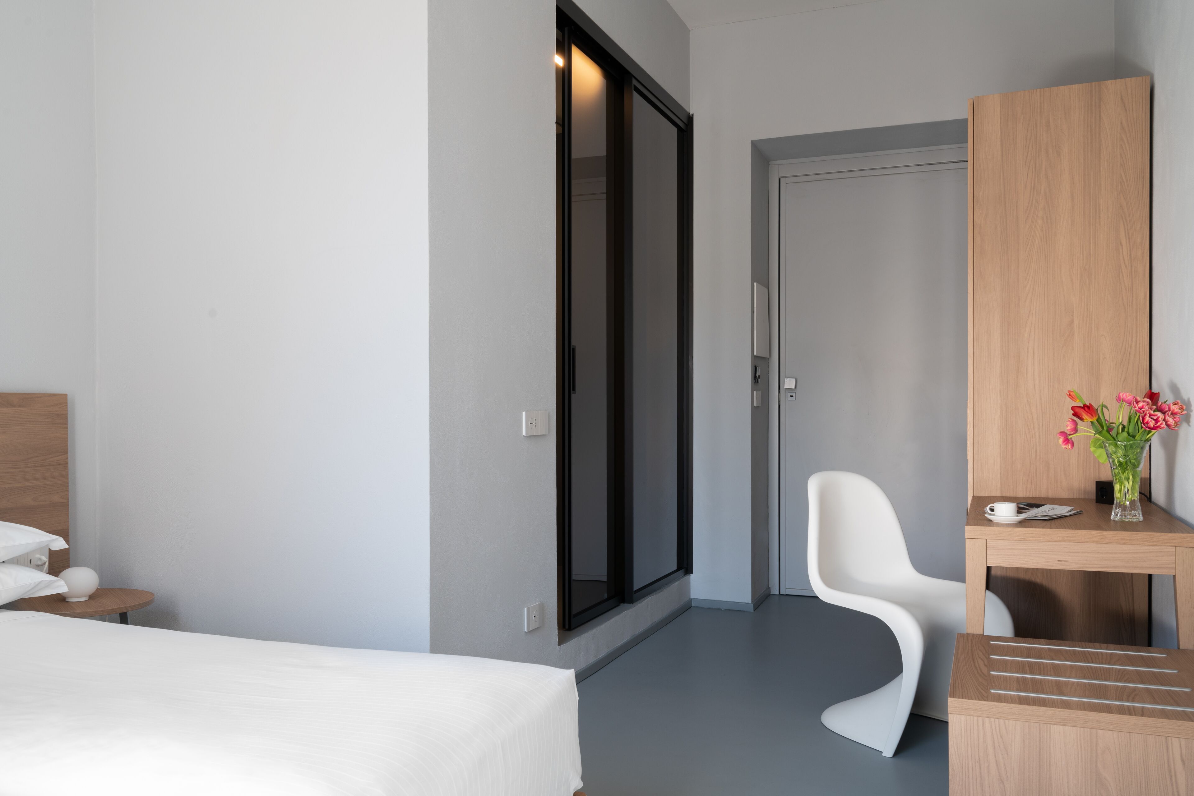Ein modernes Hotelzimmer mit einem Bett, einem Schreibtisch, einem Sessel und einer großen Schiebetür.
