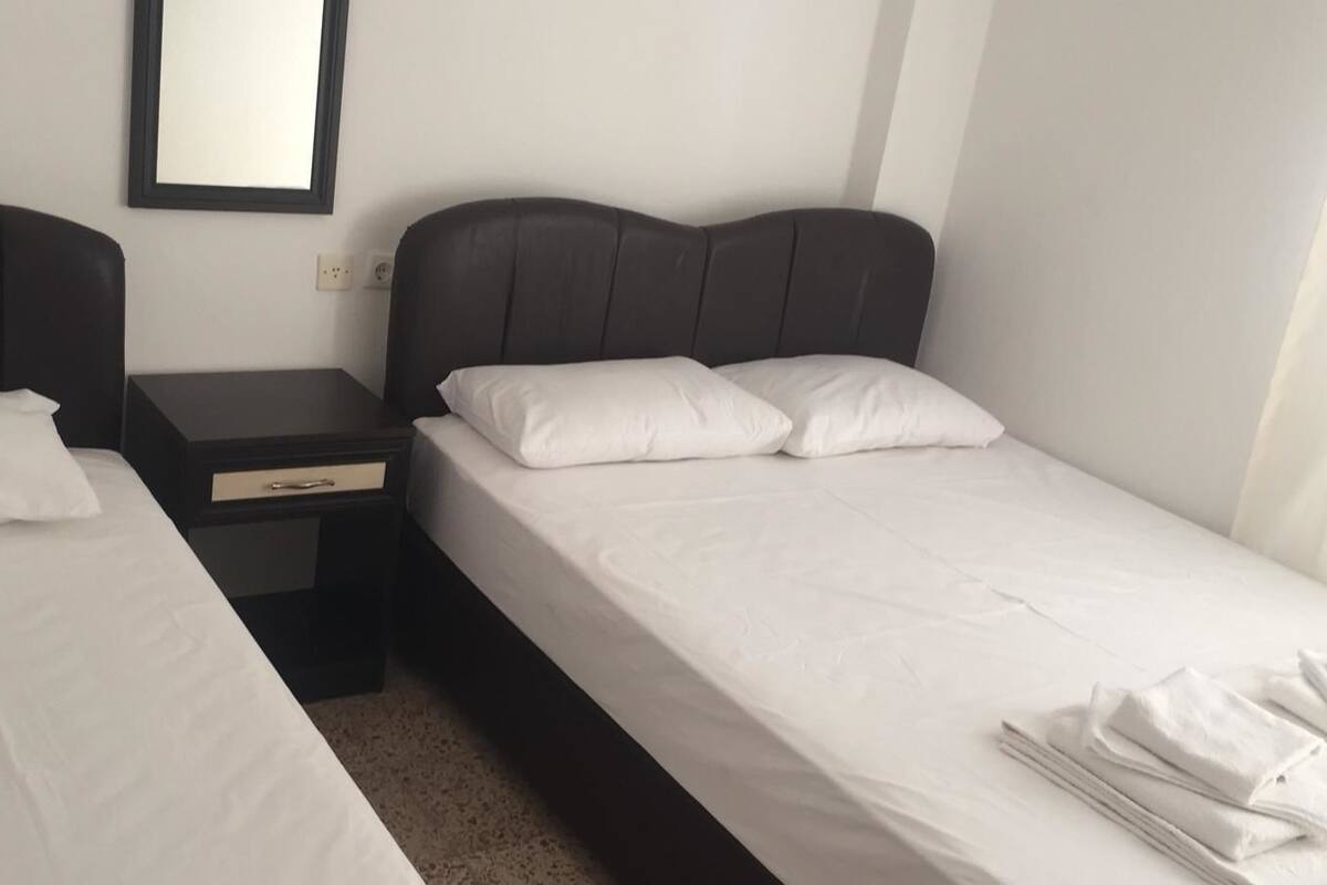 Une chambre d’hôtel avec deux lits simples, une table de chevet avec un tiroir et un miroir fixé au mur.
