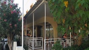 An outdoor seating area with tables and chairs, surrounded by greenery and a tree with pink flowers. - Anatolia Hotel Ozdere (Menderes)