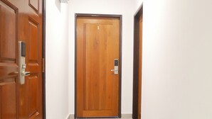 Un pasillo con puerta de madera, pared blanca y suelo de baldosas.