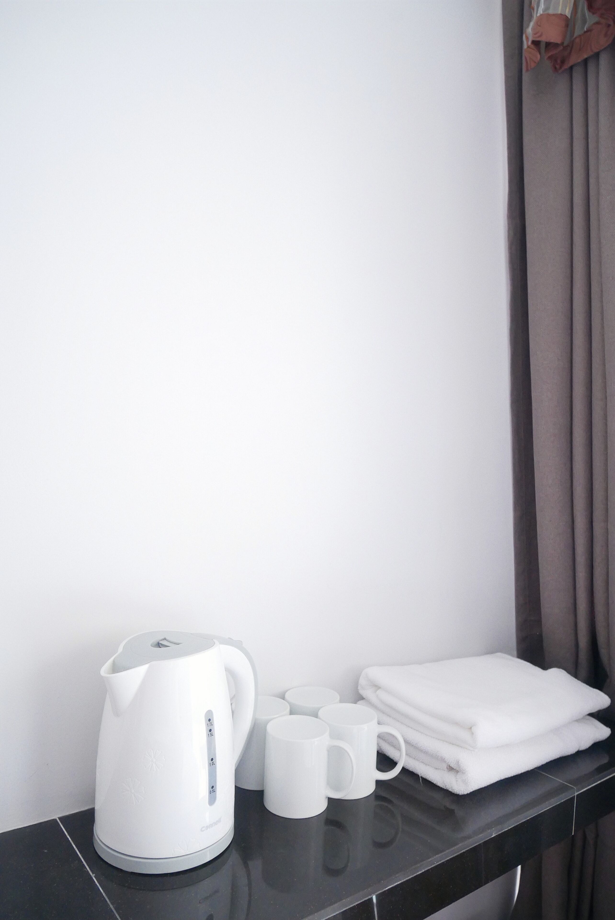 A white kettle, two white mugs, and a folded white towel on a black countertop.