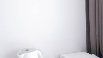 A white kettle, two white mugs, and a folded white towel on a black countertop.