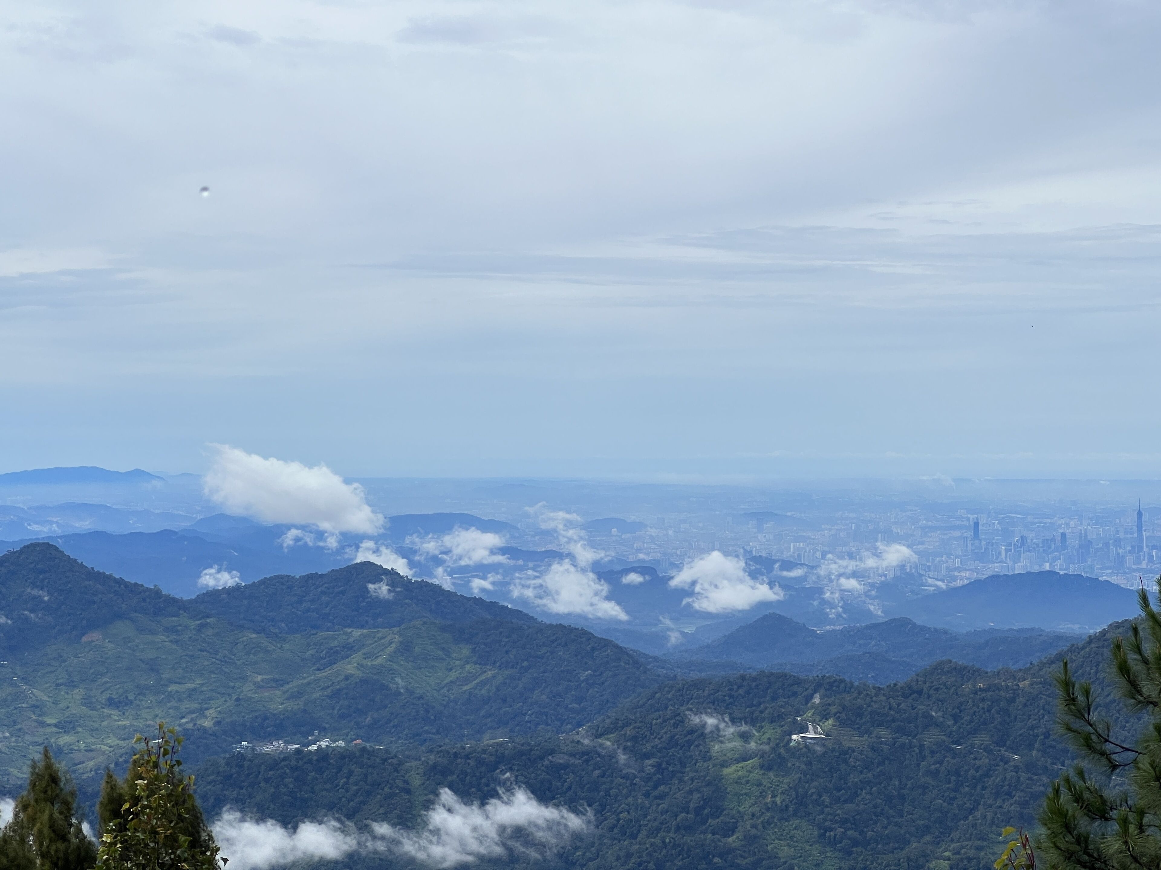 A mountainous landscape with a city in the distance, featuring rolling hills and a clear sky.