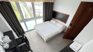 Una habitación de hotel con una cama, un escritorio con un ordenador, una silla, una cafetera y vistas a la ciudad desde la ventana.