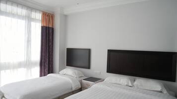 Habitación de hotel con dos camas, una mesita de noche, un televisor de pantalla plana y una ventana con cortinas translúcidas.