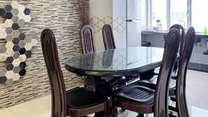 Un comedor moderno con una mesa de vidrio y sillas de madera oscura, una pared con diseño y vistas a la cocina a través de una ventana.