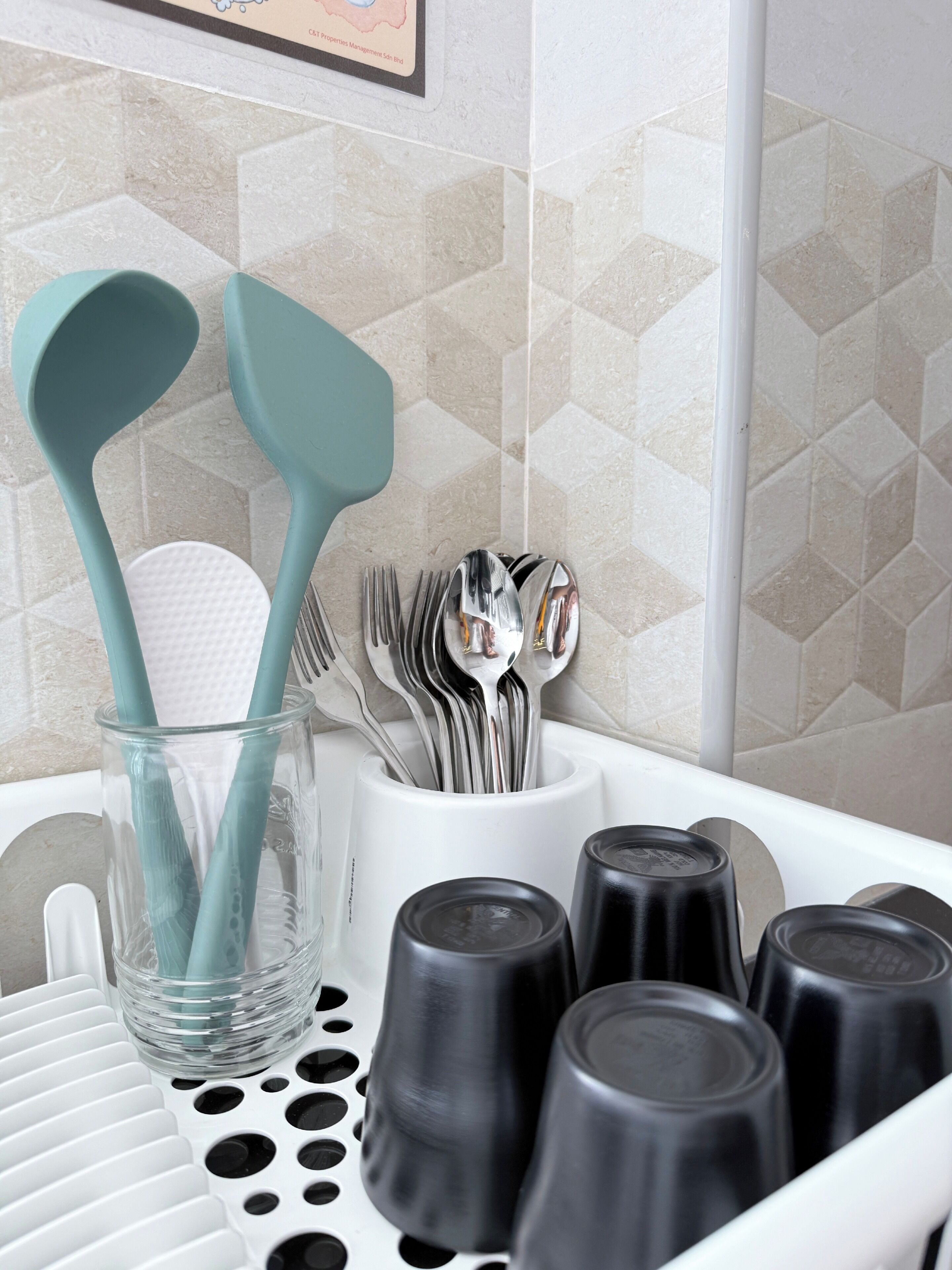 A kitchen area with a utensil holder containing spoons, forks, and a spatula, and a set of black containers on a tray.