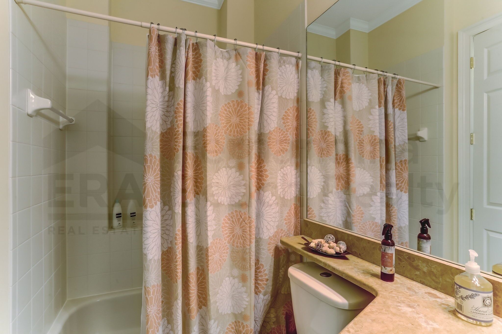 Ein Badezimmer mit Duschvorhang, Toilette, Waschbecken mit Toilettenartikeln und Spiegel.