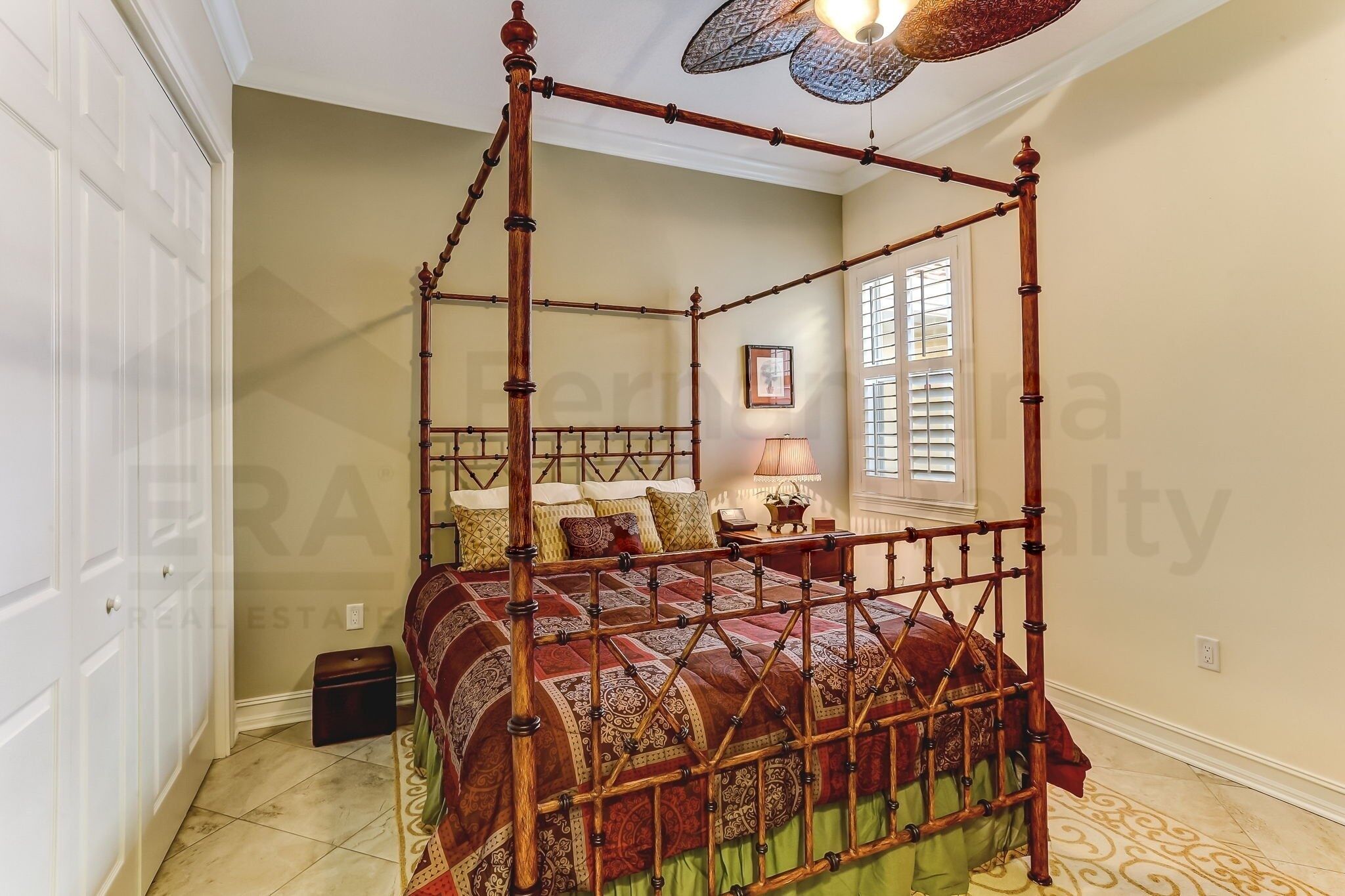 A four-poster bed with a patterned bedspread, a standing lamp, and a window with blinds.