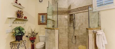 A modern bathroom with a glass-enclosed shower, a toilet, and a sink area.