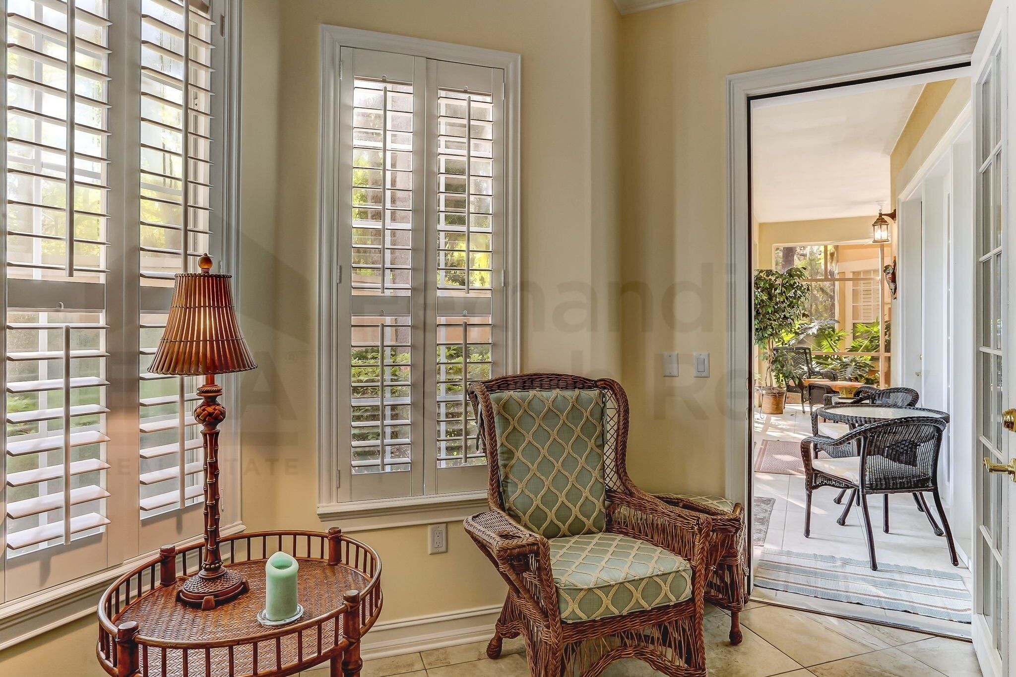 A room with a wicker chair, a table with a candle, and a window with blinds.